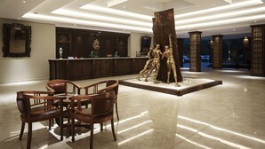A lobby with a reception desk, wooden chairs, a marble floor, and a large bronze sculpture. - The Westlake Hotel & Resort Yogyakarta (Sleman)