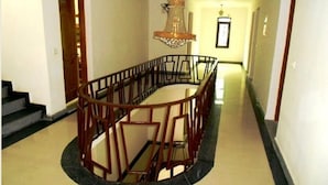 Un espacio de descanso circular con barandilla de madera, una araña y una escalera que lleva a un piso superior.