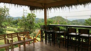 A covered outdoor seating area with wooden benches and tables, overlooking a lush landscape with hills and greenery. - Mai Ngern Mai Thong Resort (Muak Lek)