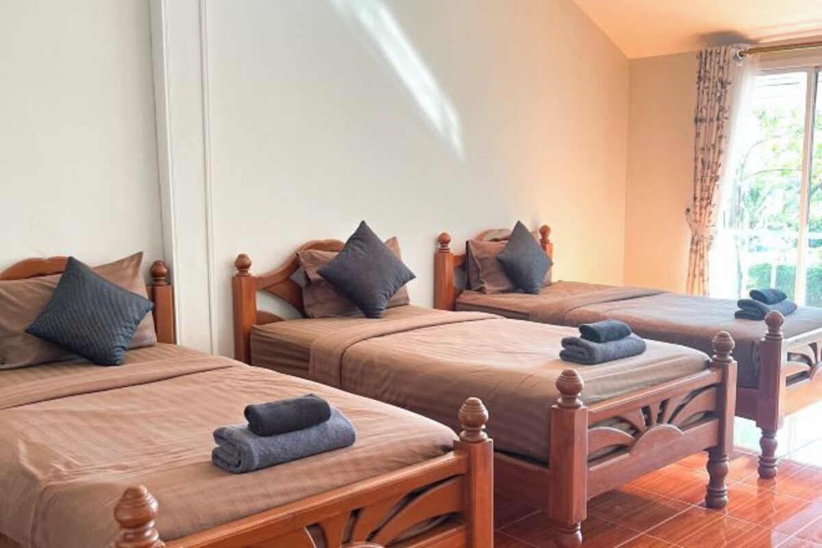 Habitación de hotel con tres camas de madera, cada una con una almohada y una toalla doblada.