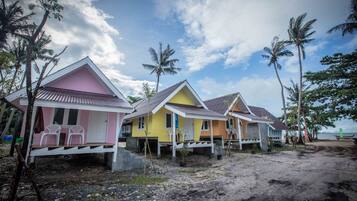 Una hilera de casas de playa coloridas con suelo de arena y palmeras.