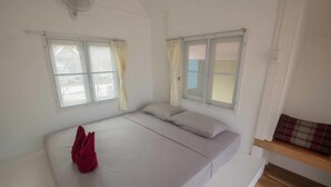 A single bed with a red towel, two windows with curtains, and a wooden bench with a patterned cushion. - The Pier Koh Phangan (Ko Pha-ngan)