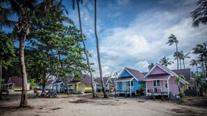 A row of colorful beach houses with a sandy ground and palm trees. - The Pier Koh Phangan (Ko Pha-ngan)