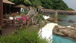 A resort with overwater bungalows, a wooden deck with outdoor seating, and a view of the ocean and lush greenery. - Gem Island Resort & Spa (Gemia Island)