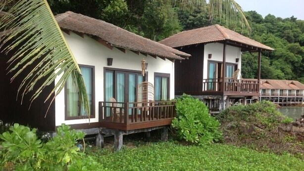 A row of bungalow-style accommodations with balconies, surrounded by lush greenery and a forested backdrop. - Gem Island Resort & Spa (Gemia Island)