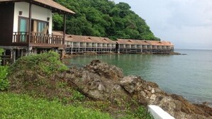 Un hotel costero con bungalows sobre el agua, un litoral rocoso y abundante vegetación en el fondo.