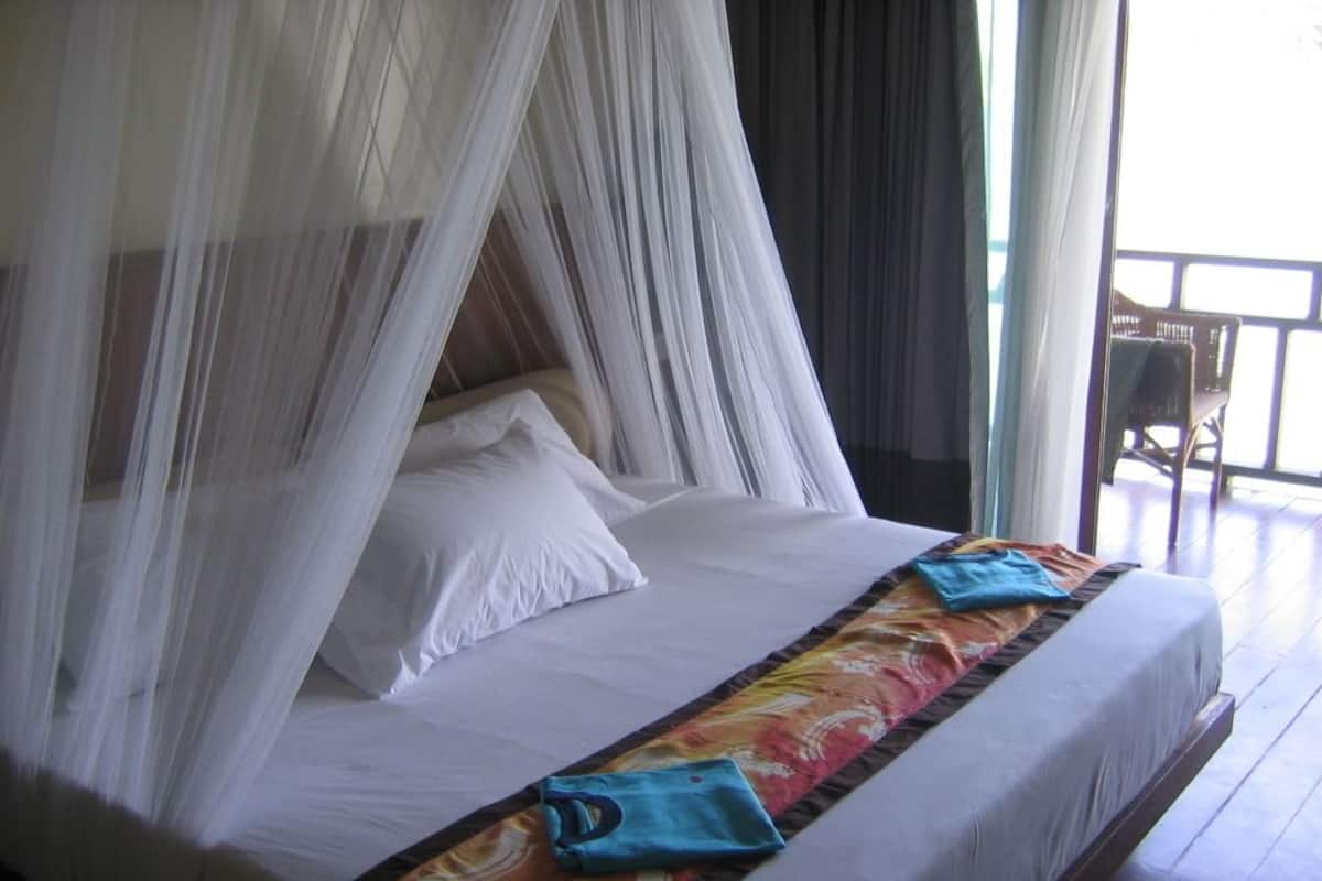 A bed with a canopy, white bedding, and a colorful blanket.