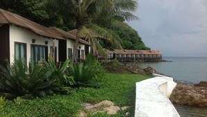 Un resort costero con bungalows sobre el agua, exuberante vegetación y un litoral rocoso.