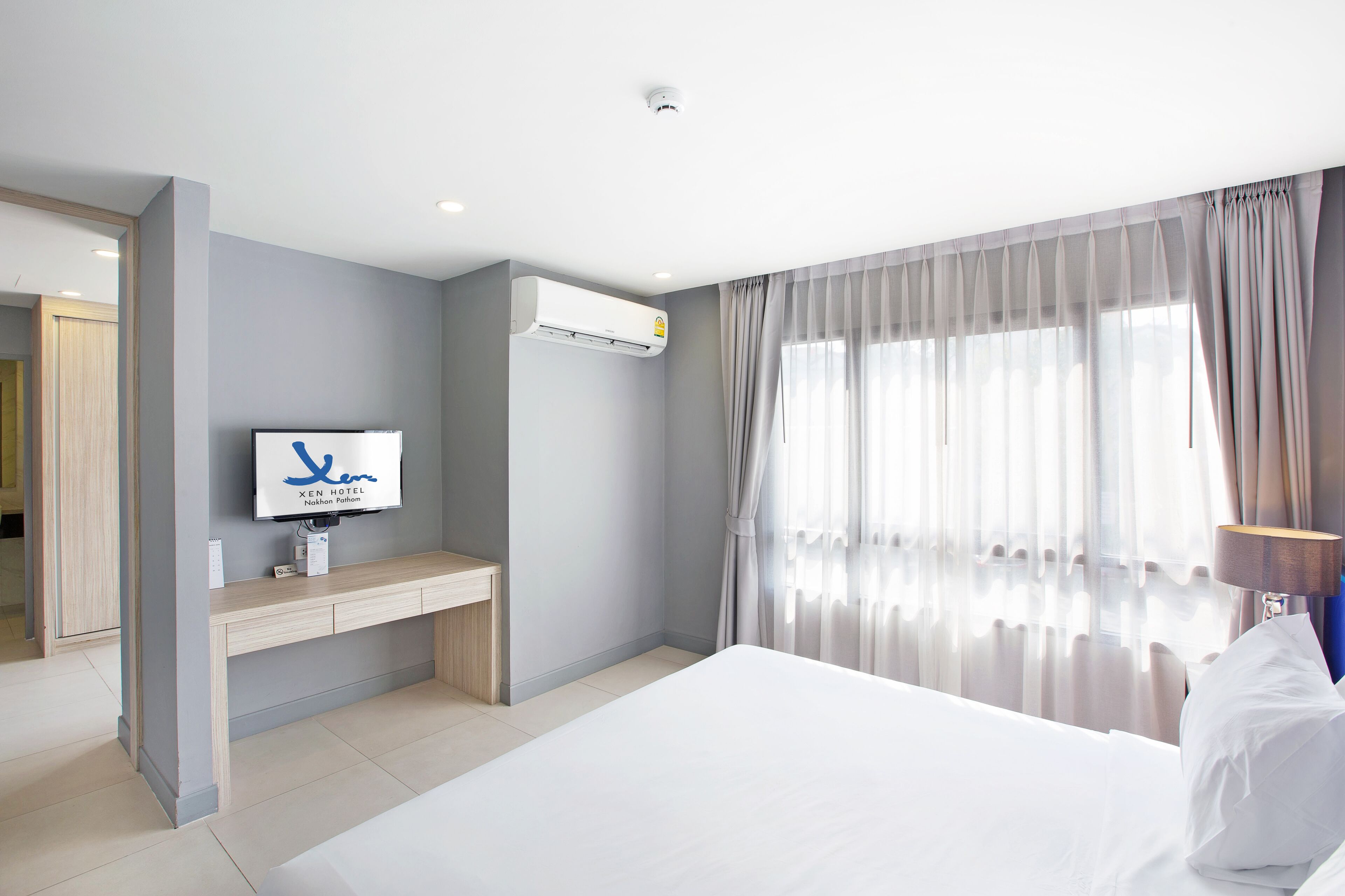 A hotel room with a bed, a TV, a desk, and an air conditioning unit.