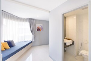 Una habitación moderna con un banco integrado, un baño con lavamanos e inodoro, y un ventanal con cortinas traslúcidas.