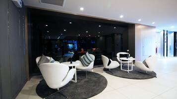 A modern lobby with white chairs and a black rug, a reception desk, and a visible bar area in the background.