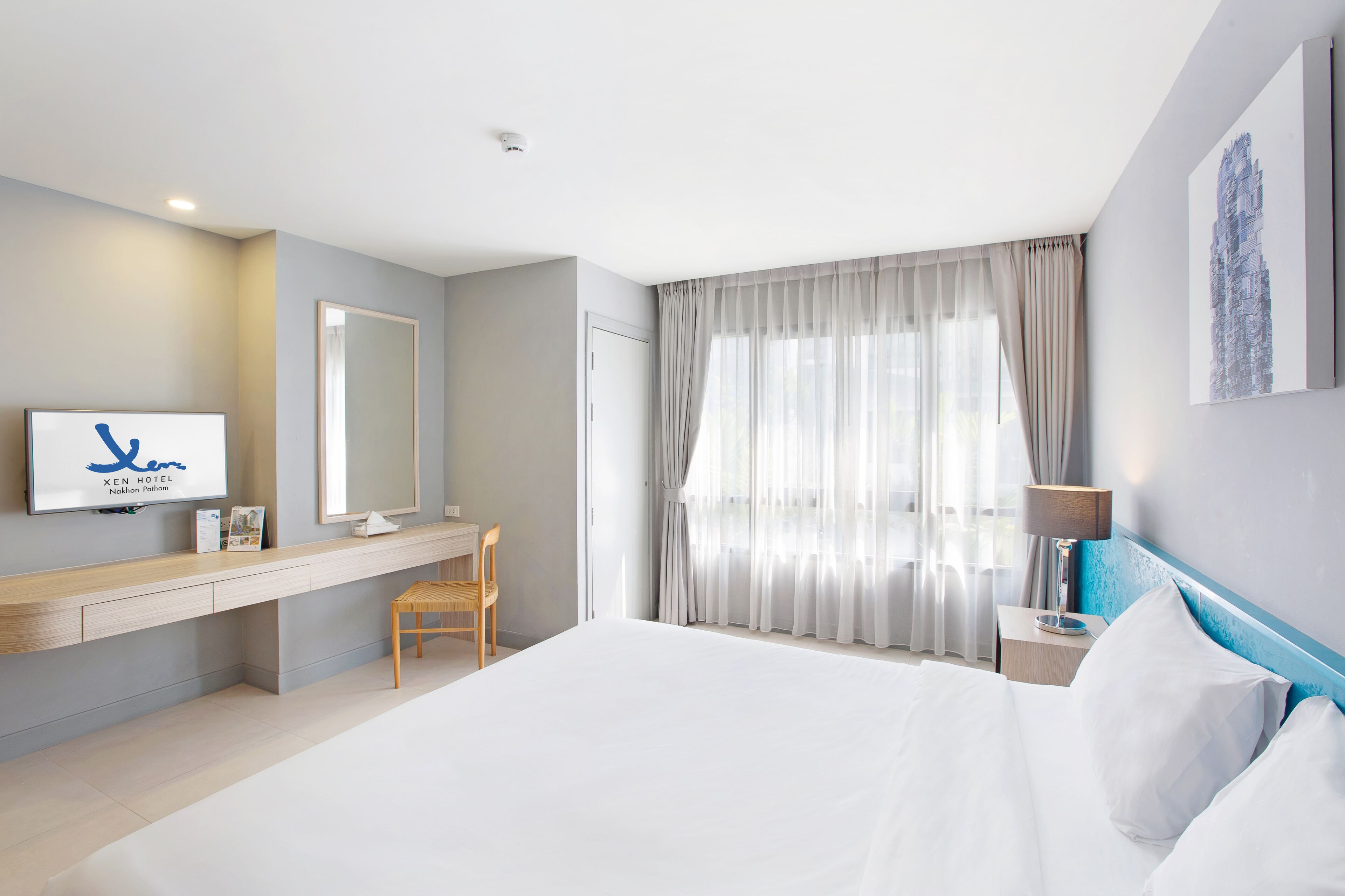 Habitación de hotel con cama, escritorio, silla, espejo, mesita de noche y ventana con cortinas.