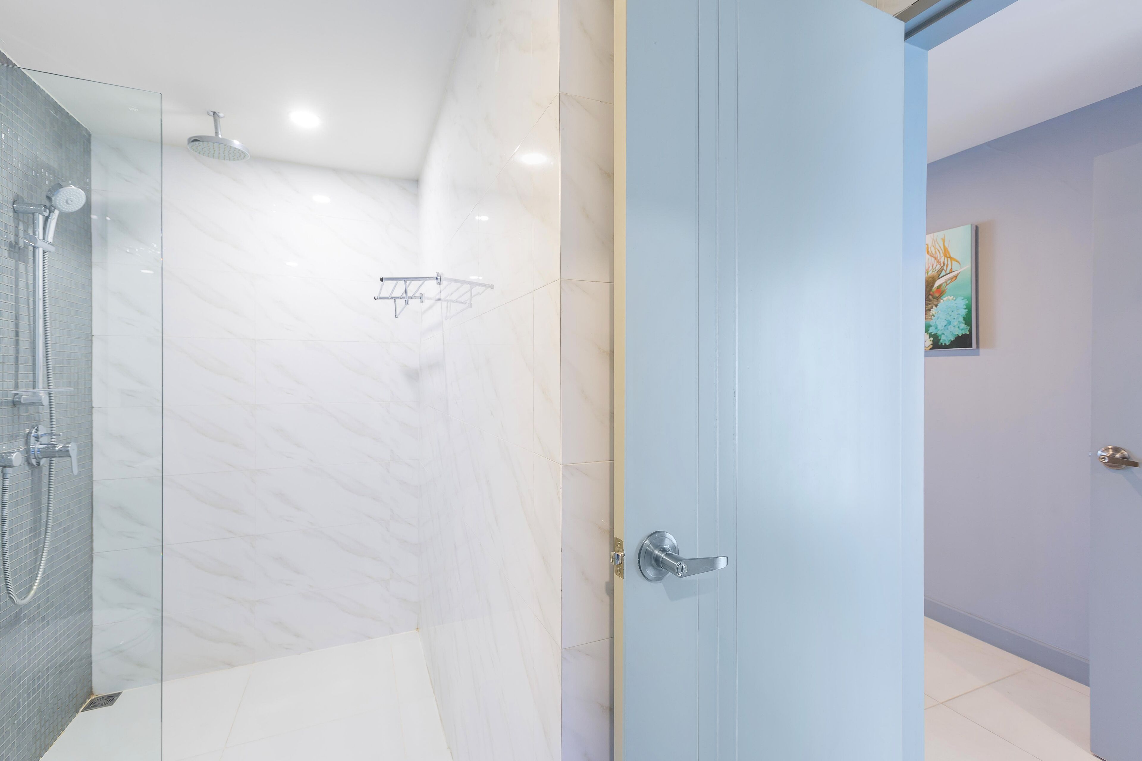 A modern bathroom with a glass shower enclosure, a towel rack, and a door with a silver handle.