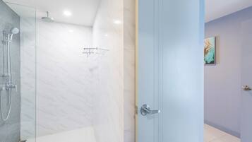 Un baño moderno con cabina de ducha de vidrio, un perchero y una puerta con pomo plateado.