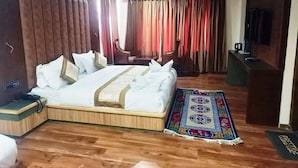 A hotel room with a large bed, a desk, a chair, a TV, and a ceiling fan.