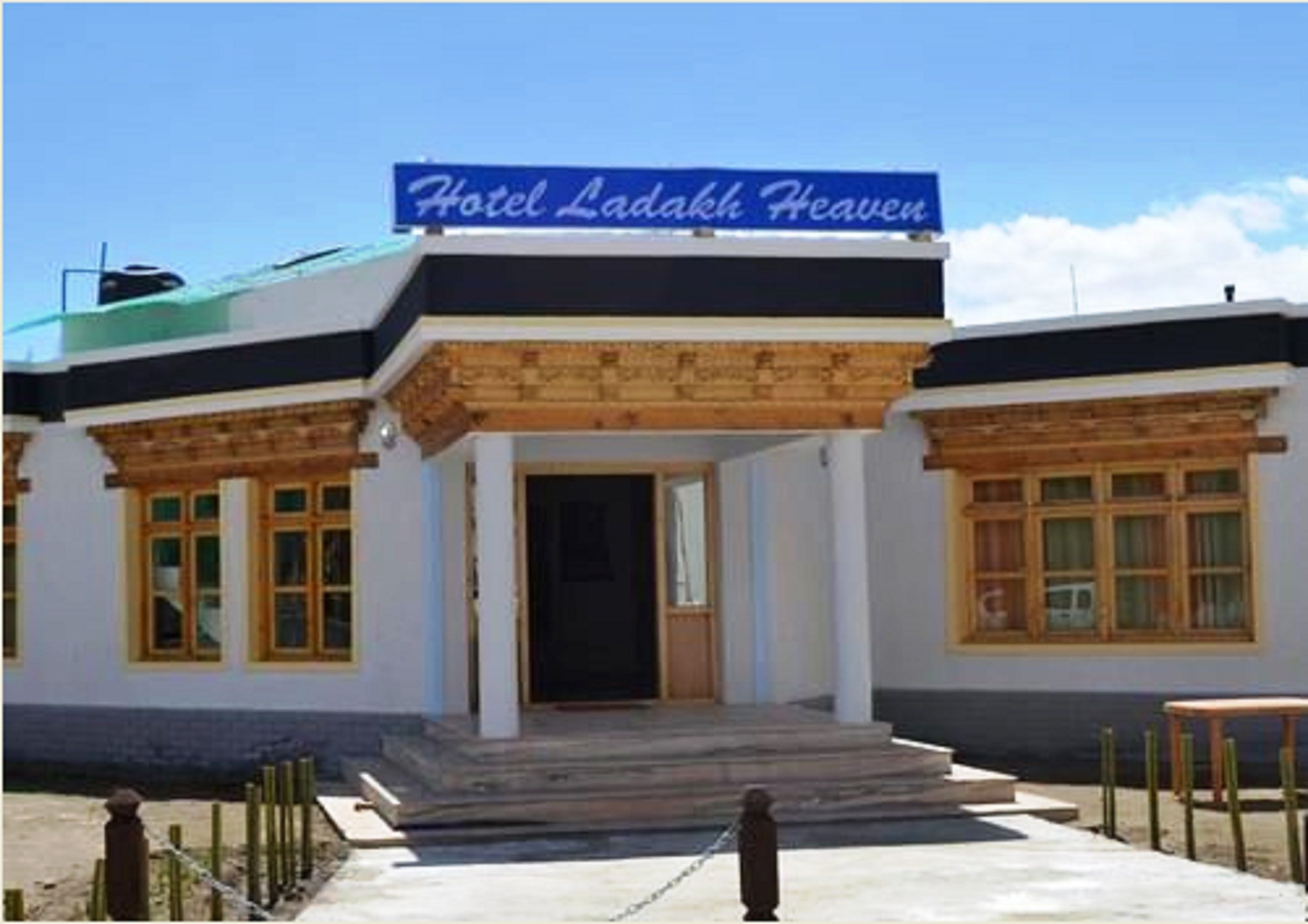 A building with a sign reading "Hotel Ladakh Heaven." It features a front entrance with steps leading up to it, wooden columns, and large windows.