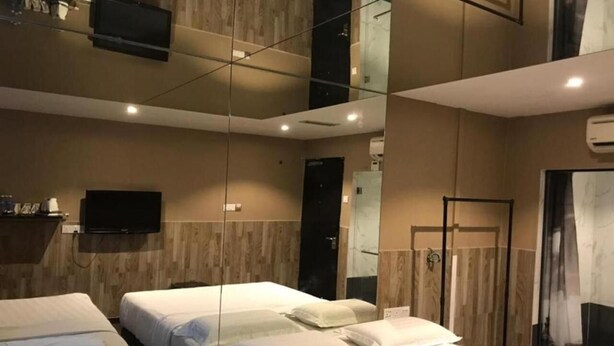 Habitación de hotel con dos camas, un televisor de pantalla plana montado en la pared y un espejo grande que refleja la habitación.