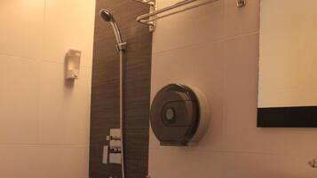 Un baño moderno con inodoro, lavamanos, toallero, cabezal de ducha y dispensador de papel higiénico en la pared.
