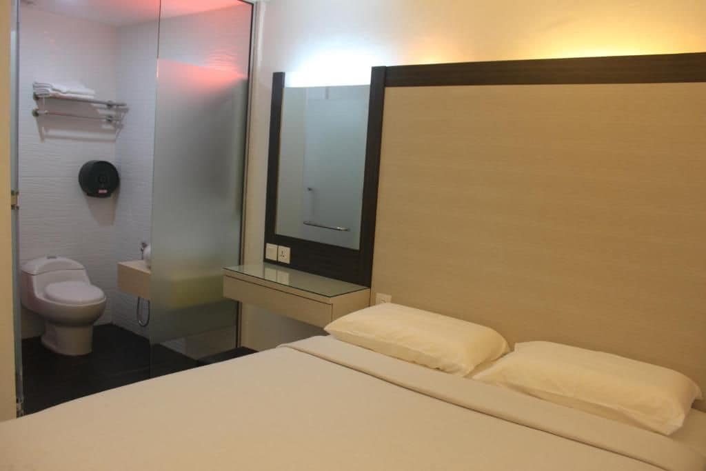 A hotel room with a bed, a mirror, a toilet, and a small bedside table.