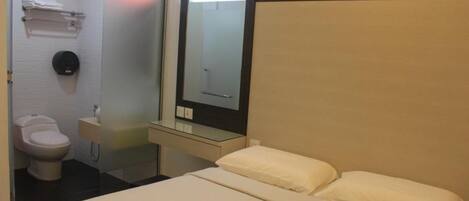A hotel room with a bed, a mirror, a toilet, and a small bedside table.