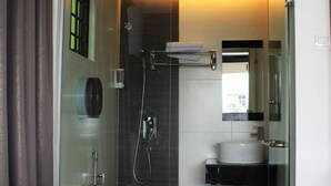 Un baño moderno con ducha envuelta en cristal, inodoro, lavamanos y espejo.