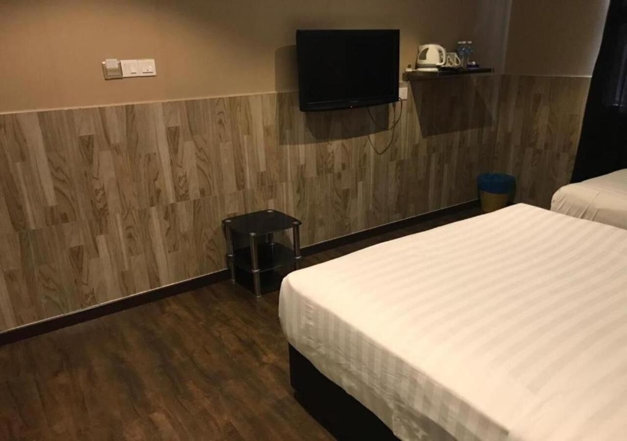 A hotel room with a wooden floor, a bed with white bedding, a television mounted on the wall, and a small trash bin.