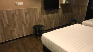 A hotel room with a wooden floor, a bed with white bedding, a television mounted on the wall, and a small trash bin.