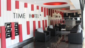 Un moderno vestíbulo de hotel con un mostrador de recepción, sofás de cuero negro y una decoración en tonos rojo y blanco.