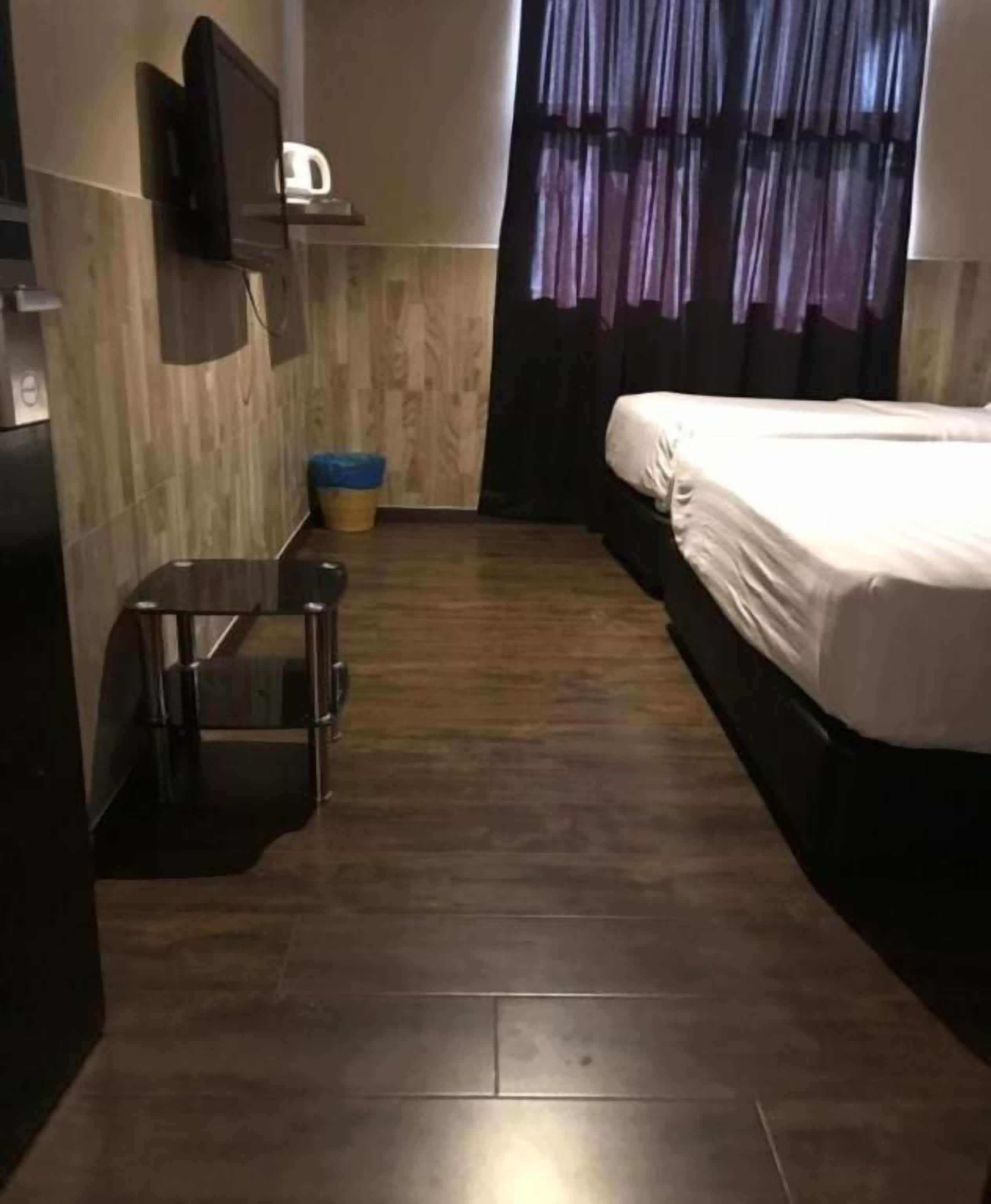 A hotel room with a bed, a small table, a TV mounted on the wall, and a window with curtains.