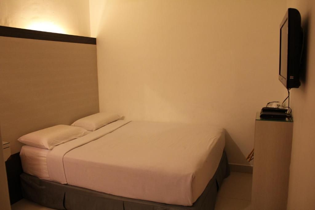 A hotel room with a bed, a flat-screen TV mounted on the wall, and a small table with a lamp.