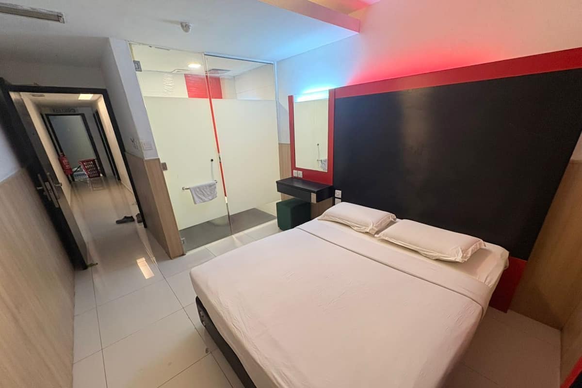 Ein Hotelzimmer mit Bett, Spiegel, Nachttisch und einer Tür zu einem Badezimmer.