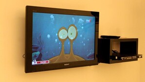 Un televisor de pantalla plana montado en una pared, mostrando un personaje animado con ojos grandes y burbujas de fondo.