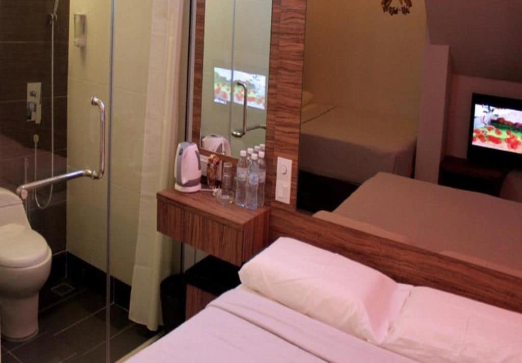 Habitación de hotel con ducha, inodoro, mesita de noche con artículos de aseo, cama y televisor.