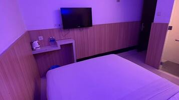 Habitación de hotel con cama, televisión, aire acondicionado y una pequeña mesa con artículos de aseo.