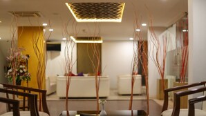 Un moderno vestíbulo de hotel con mostrador de recepción, zona de estar y elementos decorativos como jarrones altos y estilizados.