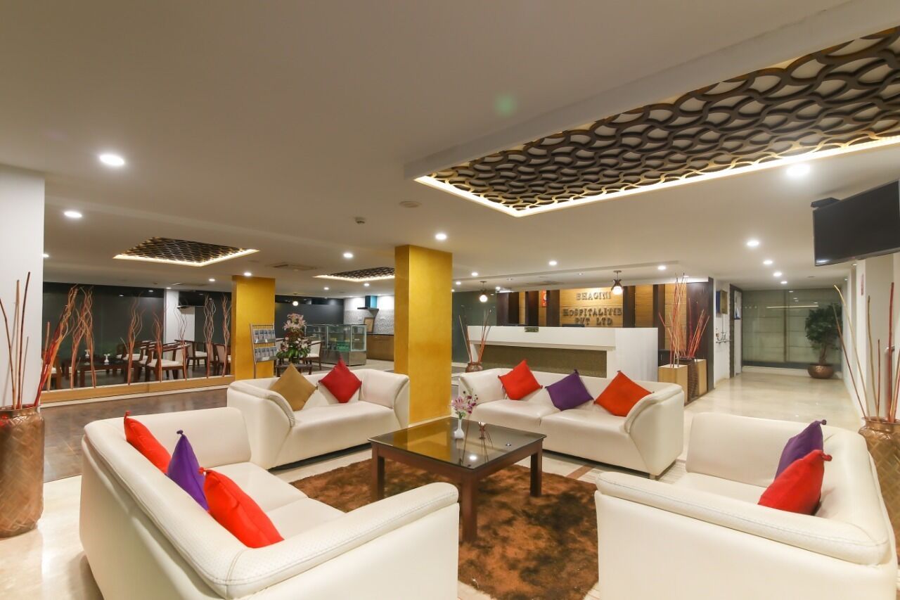 A modern hotel lobby with white sofas, a glass coffee table, and a reception desk.