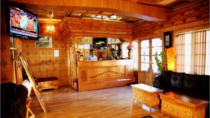 A wooden interior with a reception desk, a television, a sofa, and a patterned rug.