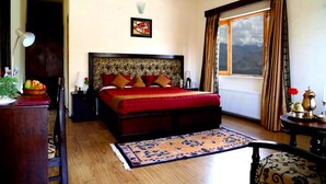 A bedroom with a large bed, a nightstand, a lamp, a window with curtains, and a view of the outdoors.