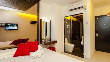 Habitación de hotel con cama, televisión, espejo, baño con ducha y puerta.