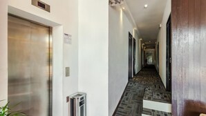 A hotel hallway with a carpeted floor, a wall-mounted elevator, and a wooden door. - Time Hotel Sunway (Petaling Jaya)