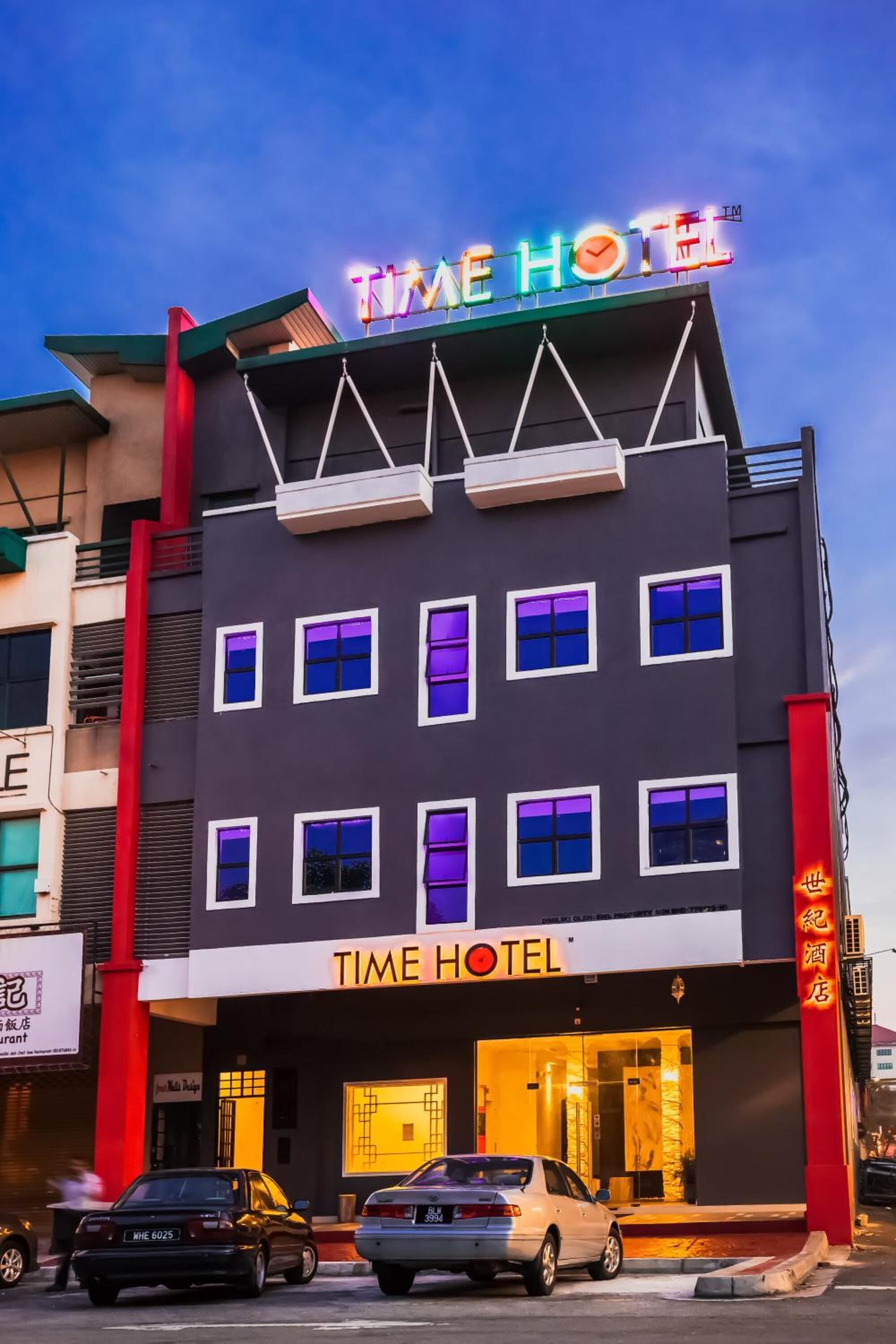 Un hotel con un letrero de neón que dice "TIME HOTEL" y un letrero vertical rojo con caracteres chinos.
