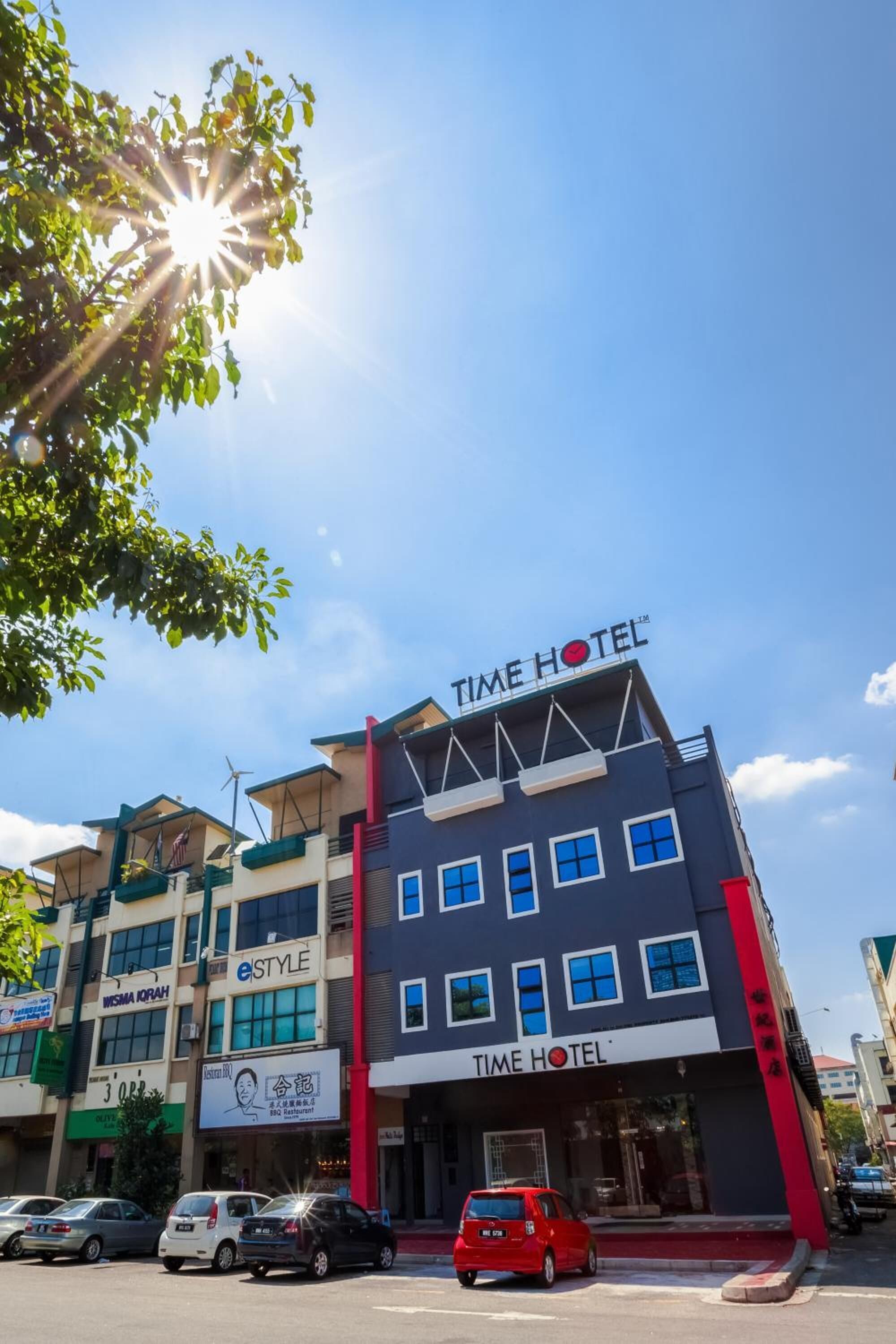 Un edificio de varios pisos con un letrero que dice 'TIME HOTEL', junto a una tienda 'eSTYLE' y el restaurante 'INSMA KOPAH'.