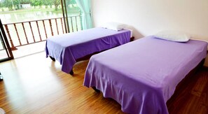 Deux lits simples avec une literie violette, dans une chambre dotée d’un plancher en bois et d’un balcon.