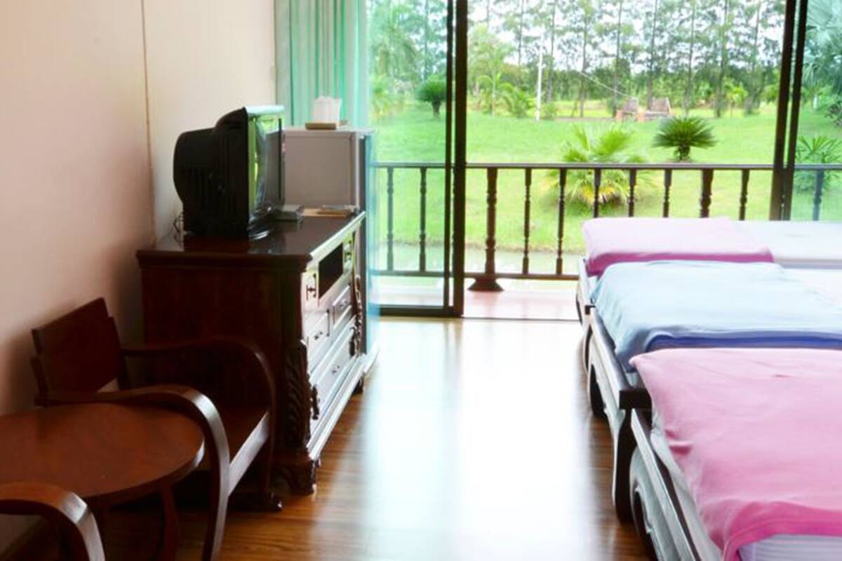 Een kamer met een houten bureau, een stoel, een televisie op een kast en een bed met roze beddengoed.