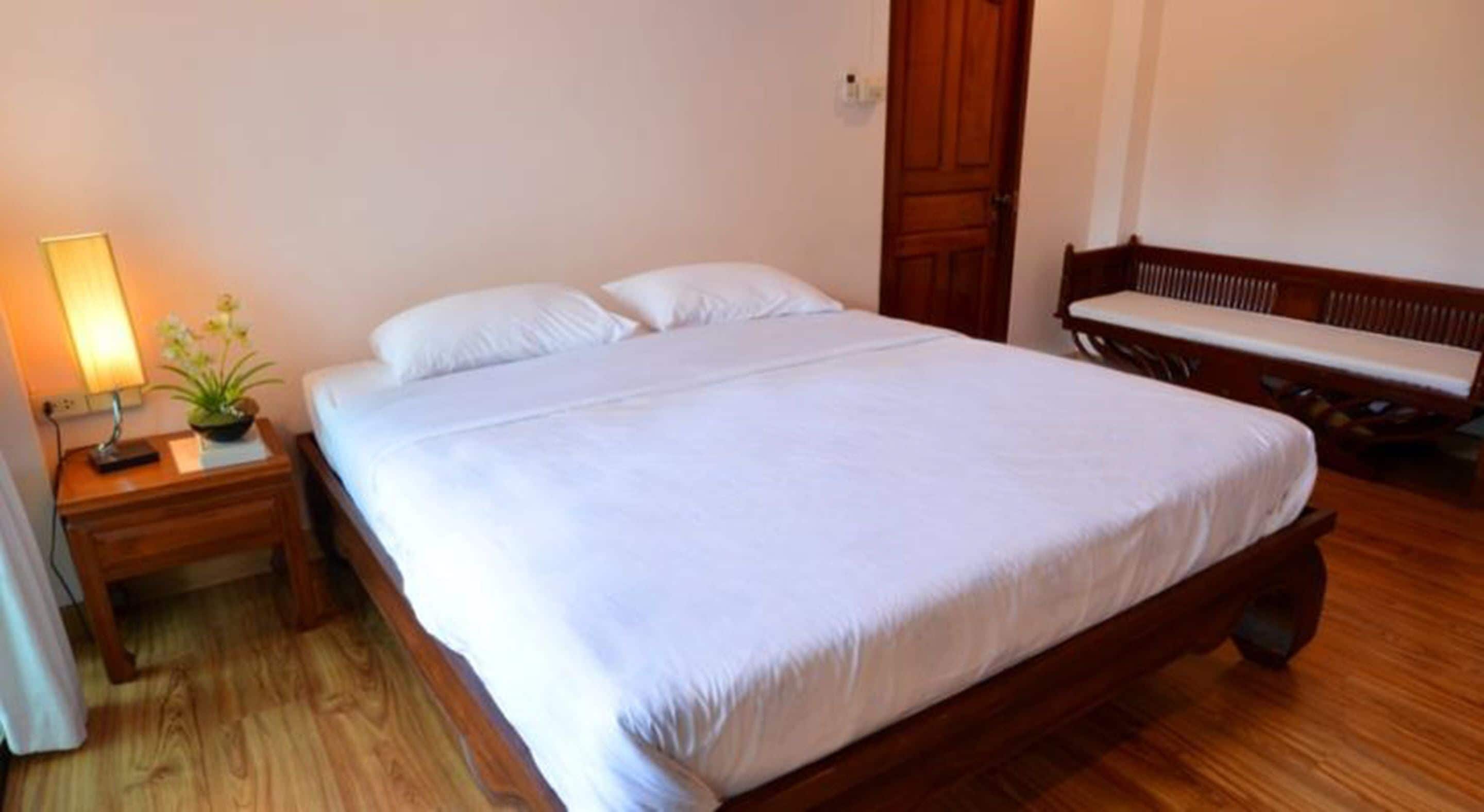 A neatly made bed with white linens in a room with wooden flooring and a wooden headboard.