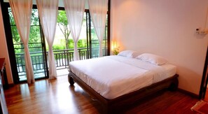 Une chambre à coucher avec un lit en bois, du linge de lit blanc et un balcon agrémenté de rideaux.