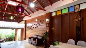 Een restaurant met een bakstenen muur, houten balken in het plafond en een zithoek met tafels en stoelen.