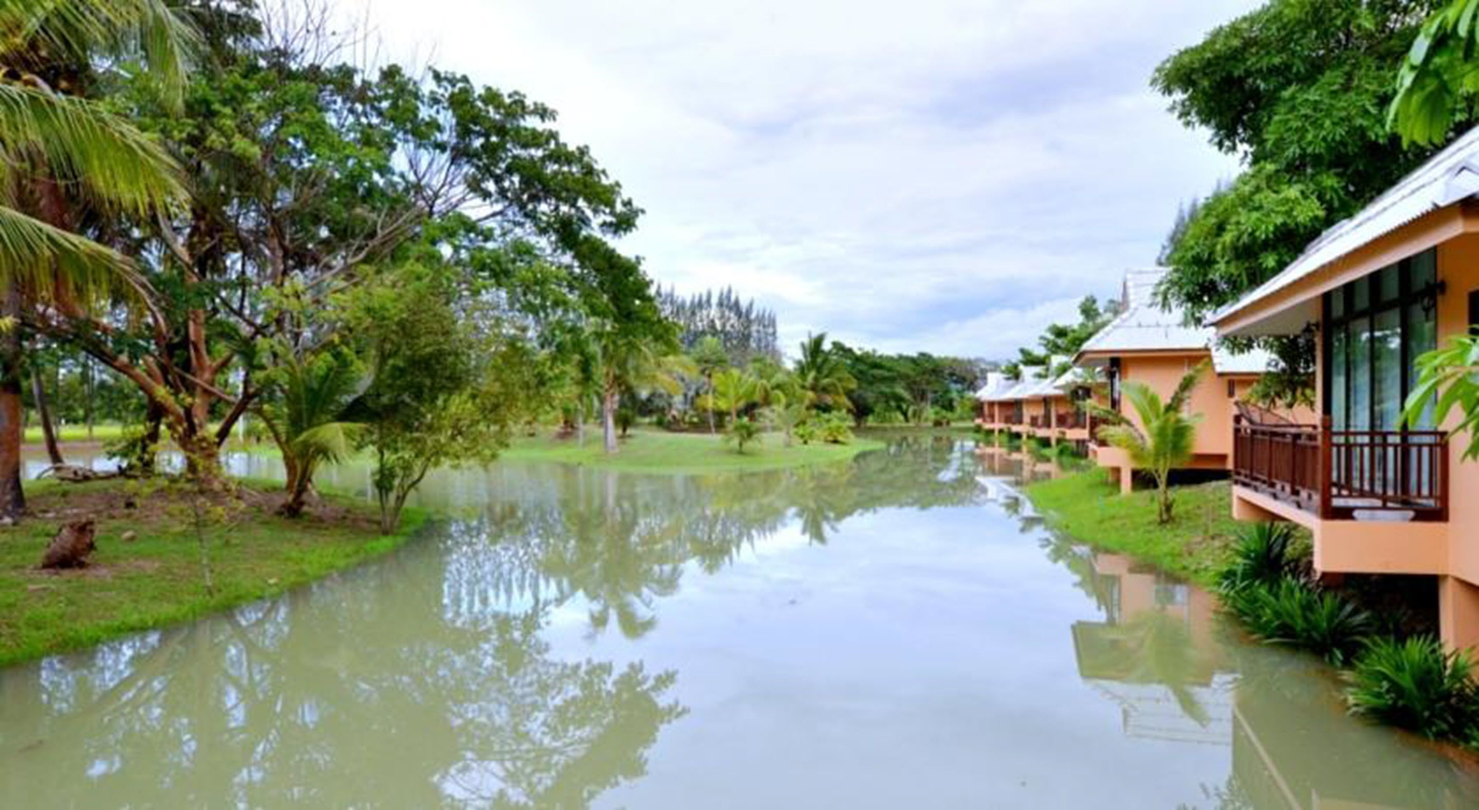 A riverside hotel with multiple guest rooms, a calm water body, and lush greenery.