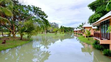 A riverside hotel with multiple guest rooms, a calm water body, and lush greenery.