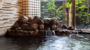 A stone waterfall feature with a tiled wall and a window overlooking greenery. - Ryokan Nagomitsuki (Beppu)